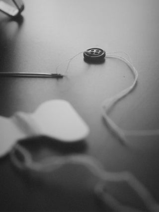 Close-up of hands repairing a small hole in a cashmere jumper with precise stitching, showcasing the craftsmanship of People's Republic of Cashmere's repair service