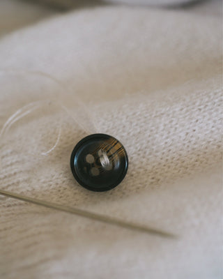 An open shipping box containing a folded cashmere jumper, with a handwritten note detailing repair instructions