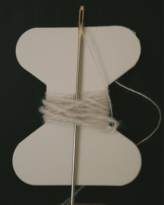Close-up of hands carefully stitching a small hole in a beige cashmere sweater, showcasing the delicate repair process